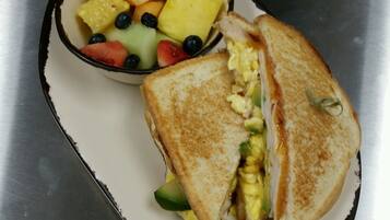 A sandwich cut in half with avocado and egg, and a bowl of fruit including strawberries, blueberries, and pineapple.