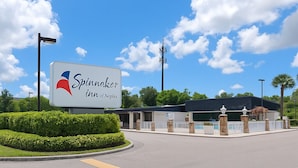 A hotel entrance with a sign for 'Spinnaker Inn of Naples,' a landscaped area with trimmed bushes, a gated entrance, and a clear sky. - Spinnaker Inn of Naples (Naples)