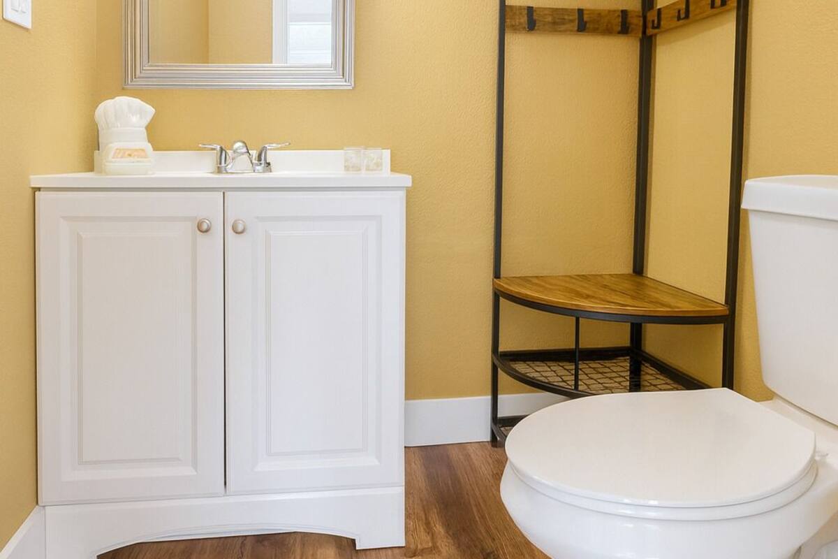 Une salle de bain avec un meuble-lavabo blanc, un miroir, des toilettes et une étagère en bois.