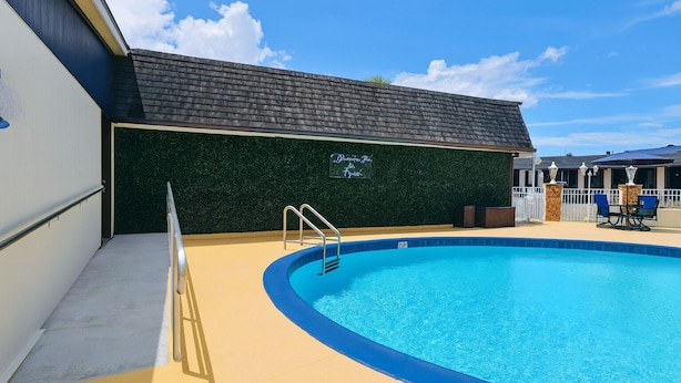 A swimming pool with a green wall and a sign, a covered patio area, and a clear sky. - Spinnaker Inn of Naples (Naples)