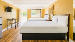 A hotel room with a large bed, a desk, a chair, a TV, and a window with blinds. - Spinnaker Inn of Naples (Naples)