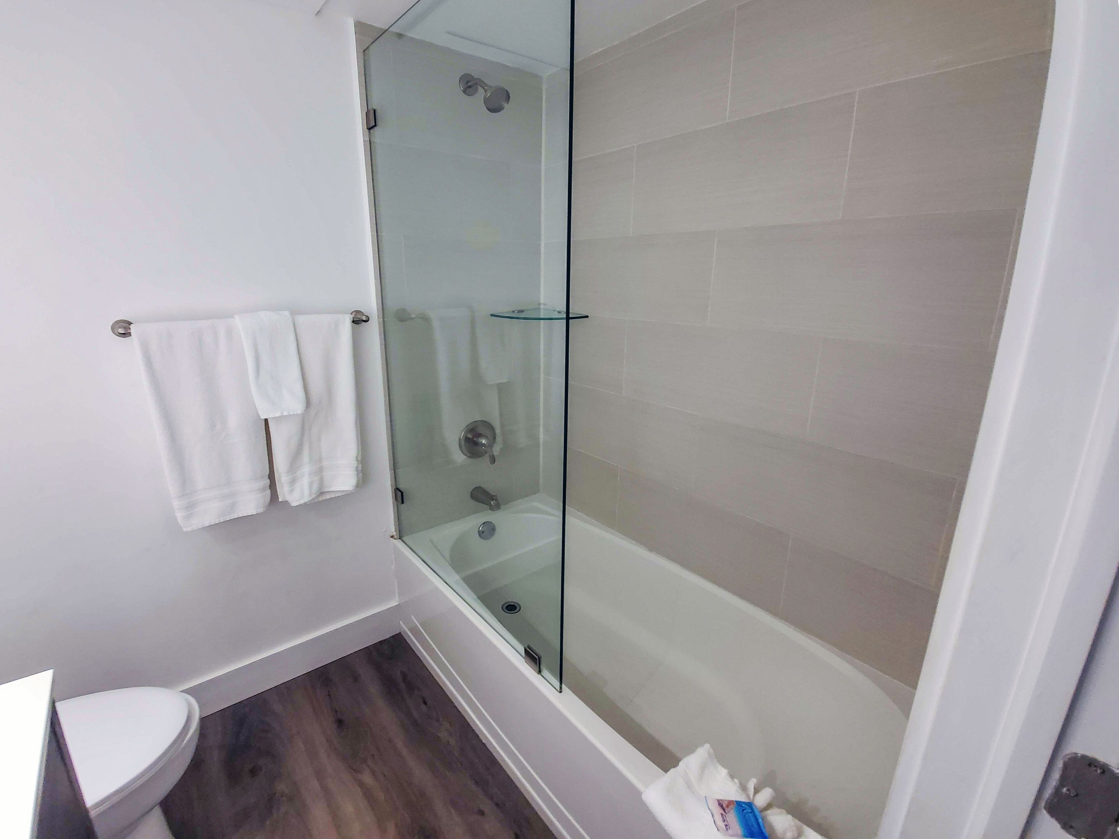 Un baño con cabina de ducha de vidrio, inodoro y estante de vidrio.