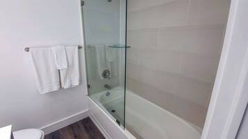 Un baño con cabina de ducha de vidrio, inodoro y estante de vidrio.