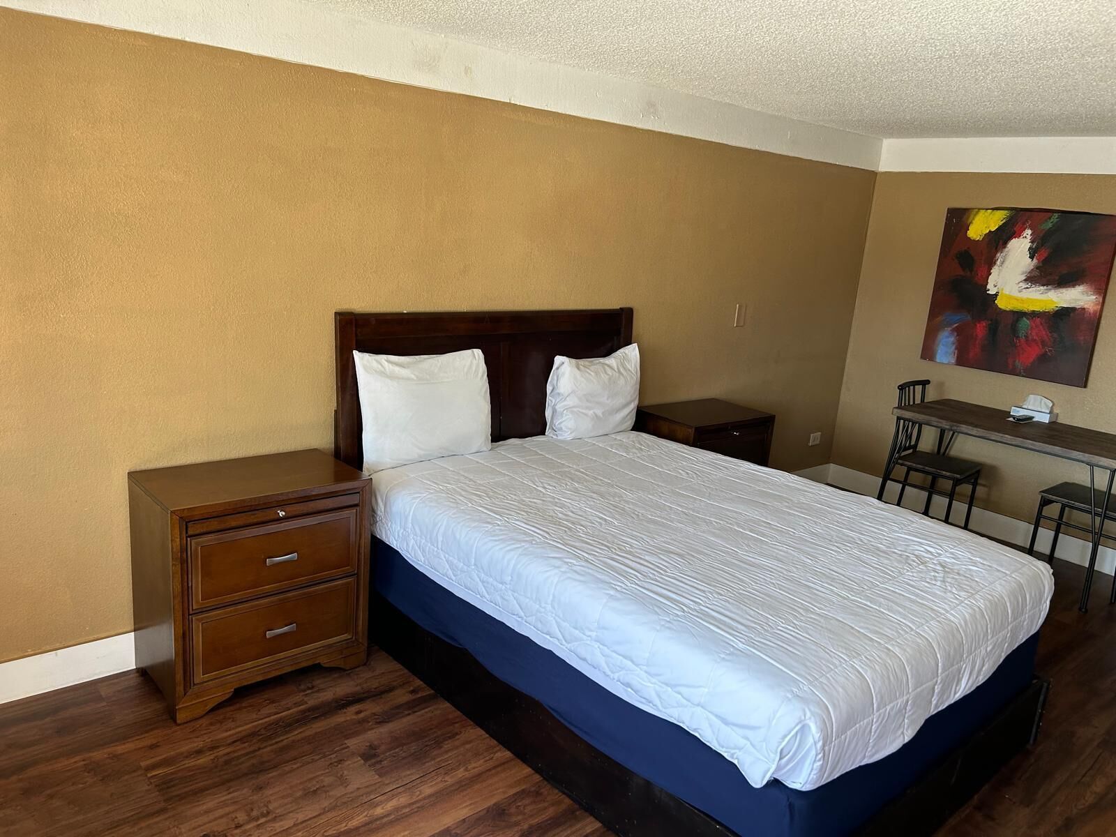Ein Hotelzimmer mit einem Bett, einem Nachttisch aus Holz, einem Schreibtisch und einem Sessel.