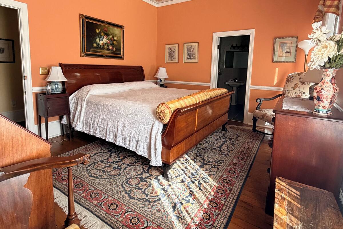 Een slaapkamer met een bed, een plafondventilator, een vloerkleed, een dressoir en een stoel.