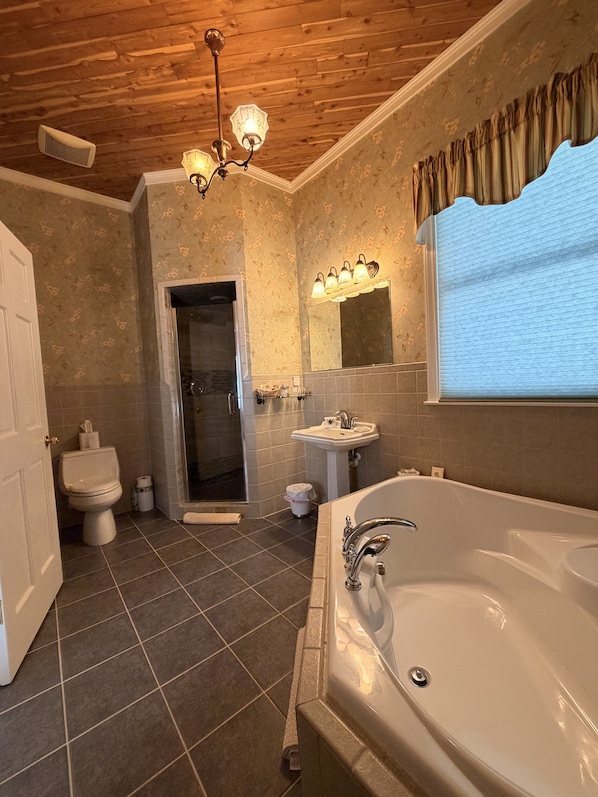 A bathroom with a wooden ceiling, a large bathtub, a shower, and a sink.
