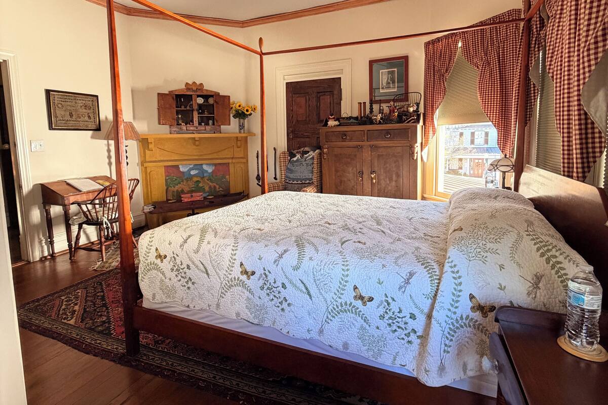Een slaapkamer met een hemelbed, houten meubels, een bureau en een stoel.