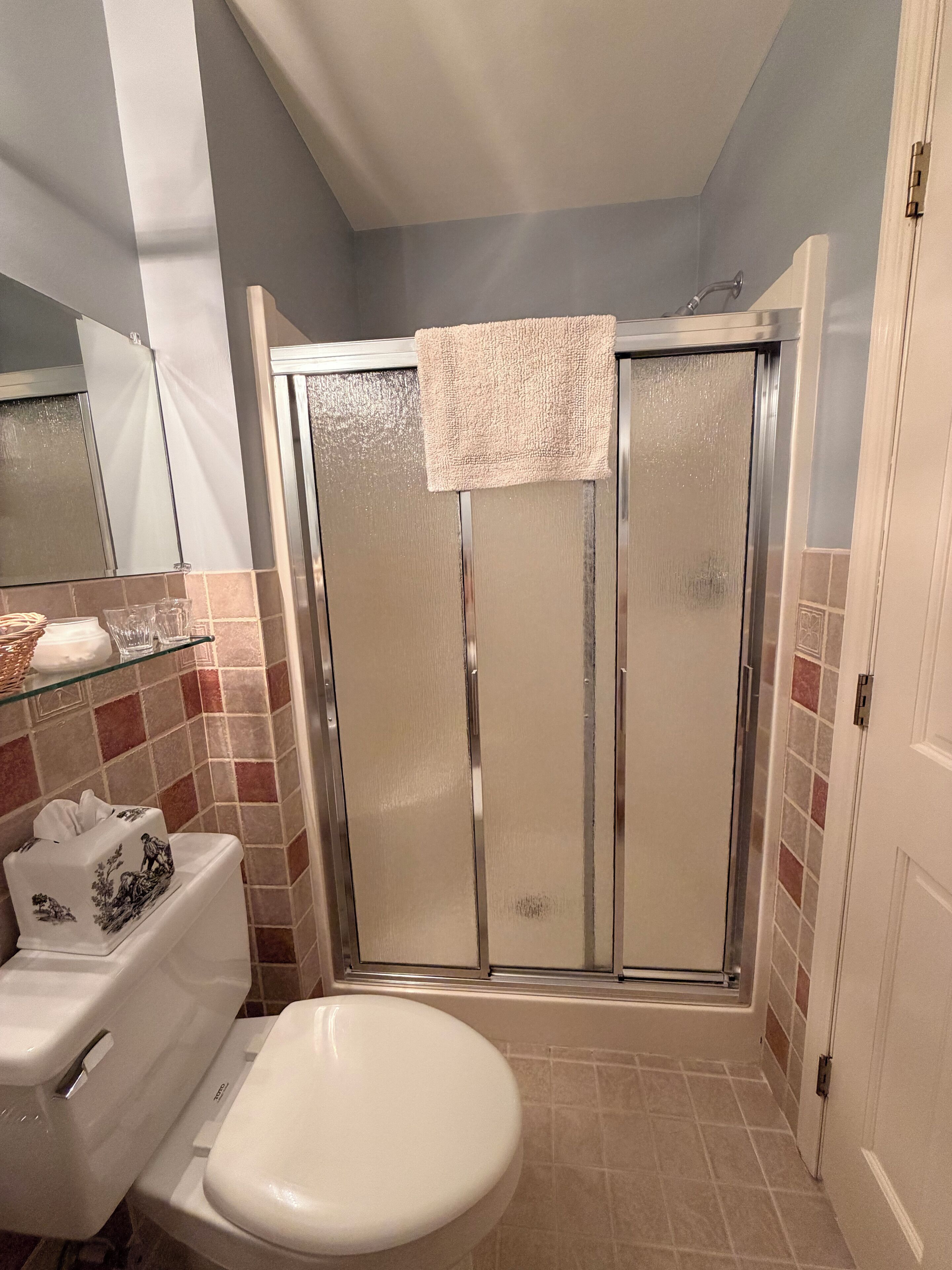 A bathroom with a toilet, a glass shower enclosure, and a tiled floor.