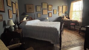 Een klassieke slaapkamer met een groot bed, een houten hoofdbord, een plafondventilator en een raam met gordijnen.