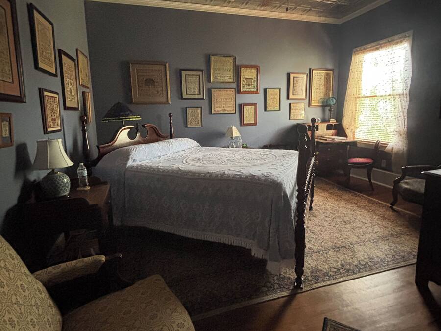 A traditional bedroom with a large bed, a wooden headboard, a ceiling fan, and a window with curtains.