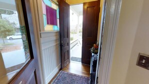 Een gang met een houten deur, een raam met uitzicht op een straat en een tapijt op de vloer.