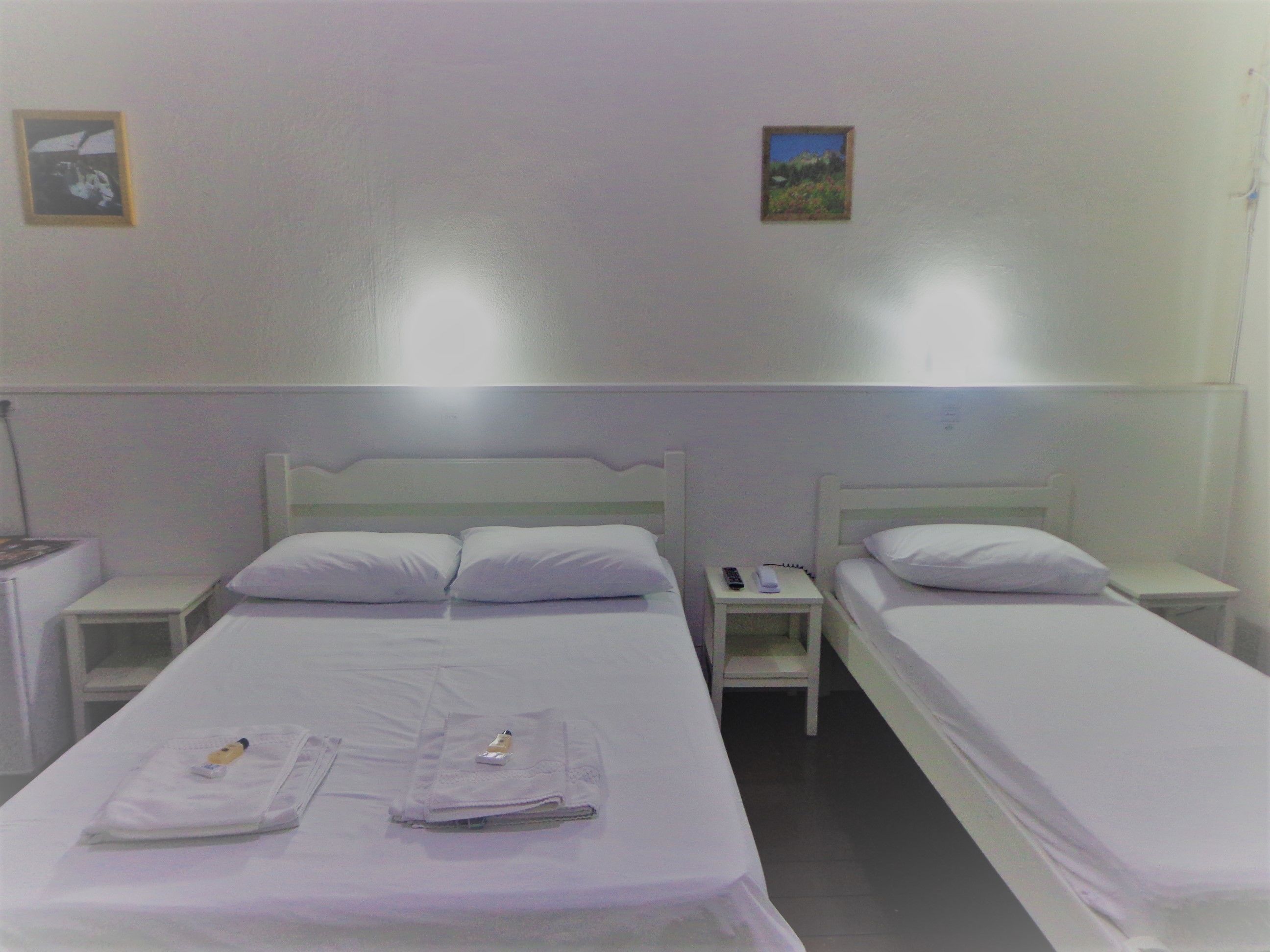 A hotel room with two single beds, white bedding, a nightstand with a lamp, and a small picture on the wall.