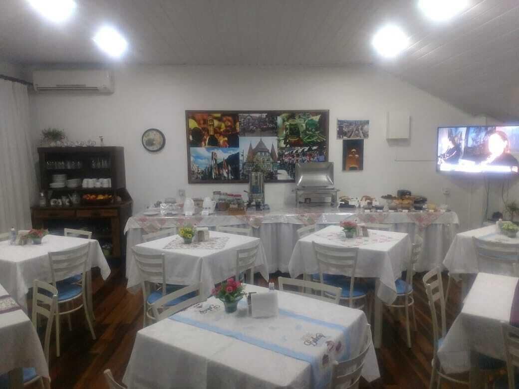 Un comedor con mesas redondas cubiertas con manteles blancos, sillas y una barra de servicio.