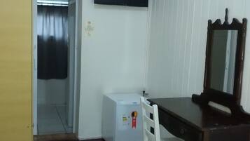 Quarto de hotel com cama, escrivaninha com cadeira, televisão fixada na parede e um pequeno frigorífico.