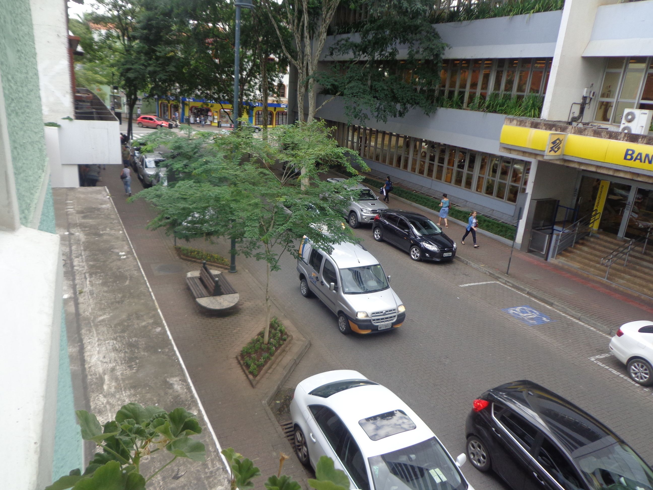 Une vue de rue avec des voitures garées, un banc et un bâtiment portant l’inscription « Banque ».
