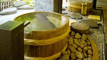 A traditional Japanese onsen with wooden tubs and a stone wall.