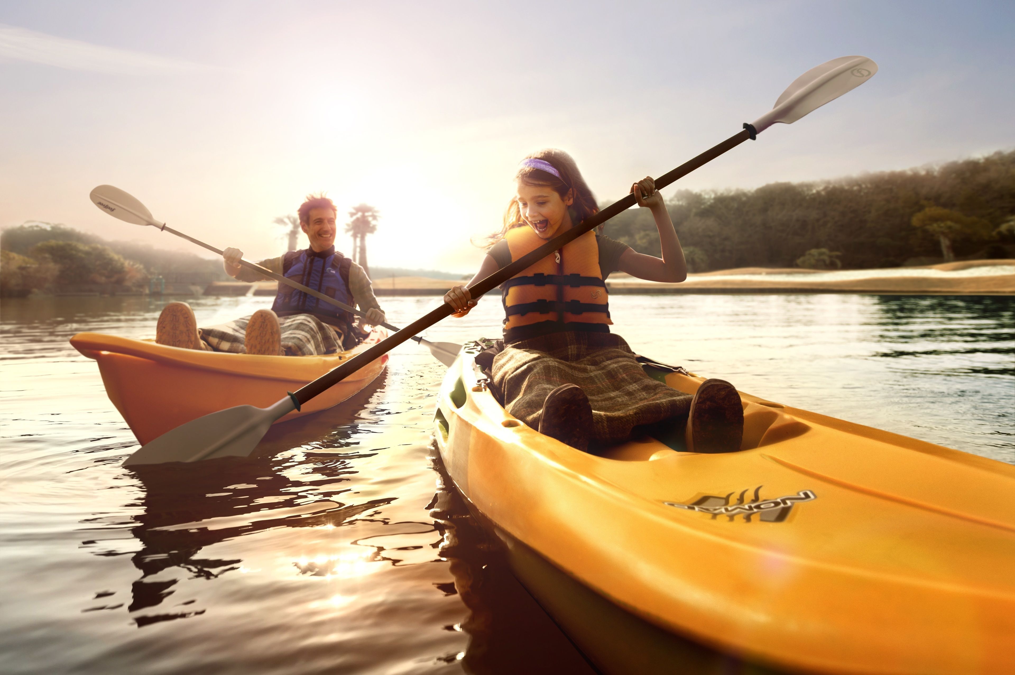 Two people kayaking on a calm river with a forested shoreline in the background.