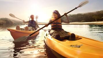 Two people kayaking on a calm river with a forested shoreline in the background.