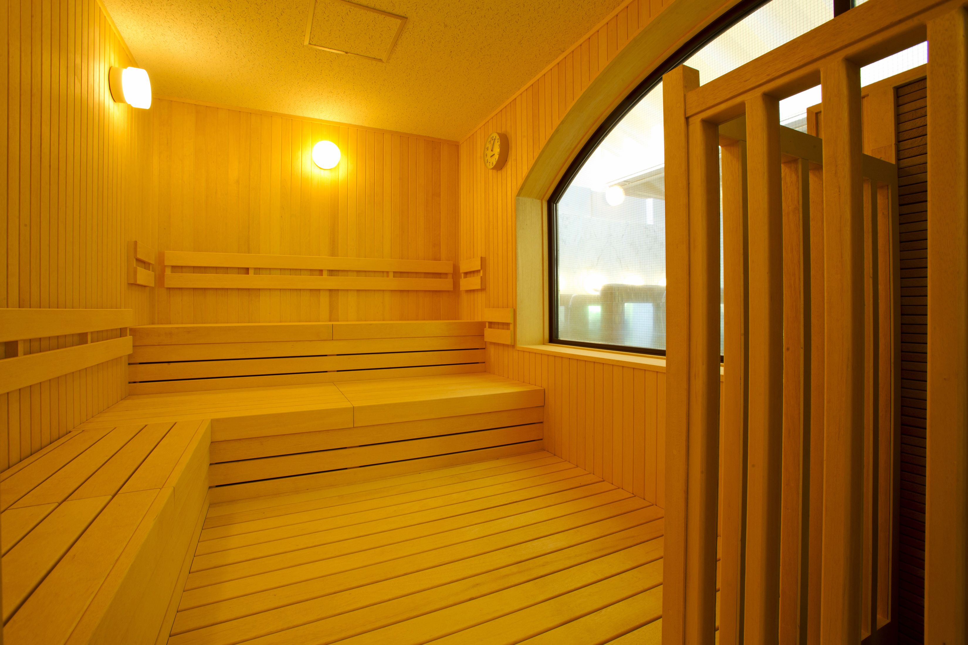 A wooden sauna with benches and steps, a clock on the wall, and a window.