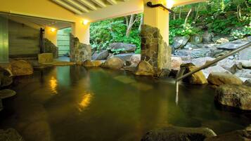 A hot spring area with a stone pool, rocks, and a wooden staircase.