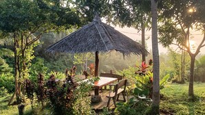 A rustic outdoor seating area with a thatched roof, surrounded by lush greenery and tropical plants. - Erlittop Nature Lodge (El Nido)