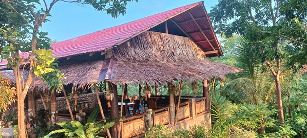 Une construction rustique en bois, dotée d’un toit de chaume et entourée d’une végétation luxuriante.