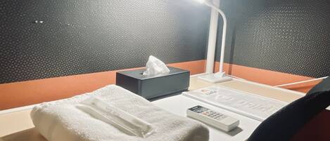 A hotel room with a bed, a bedside table, a lamp, a tissue box, a remote control, and a wall with a textured pattern.