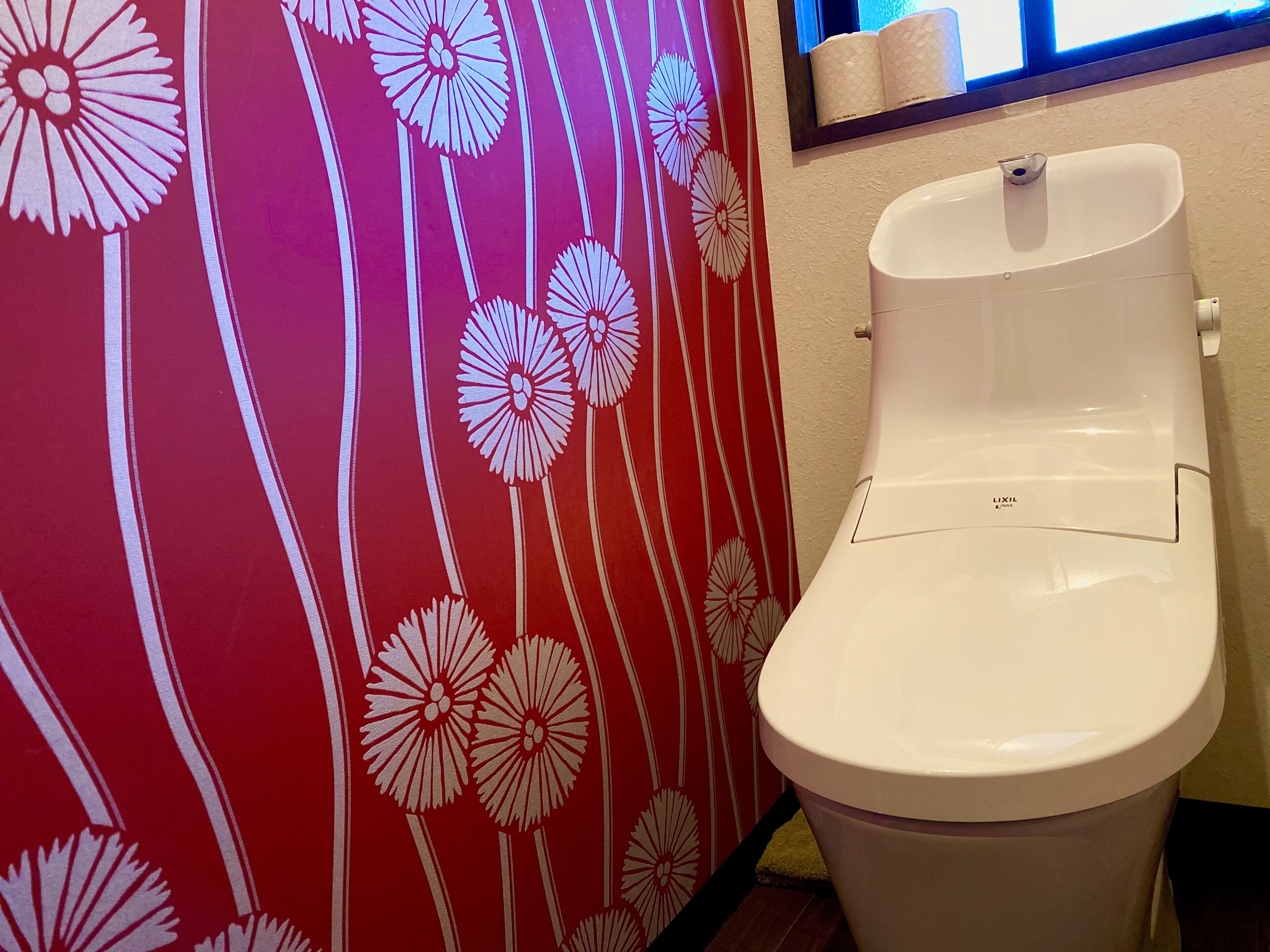 A toilet with a white lid and a wall with a red floral pattern.
