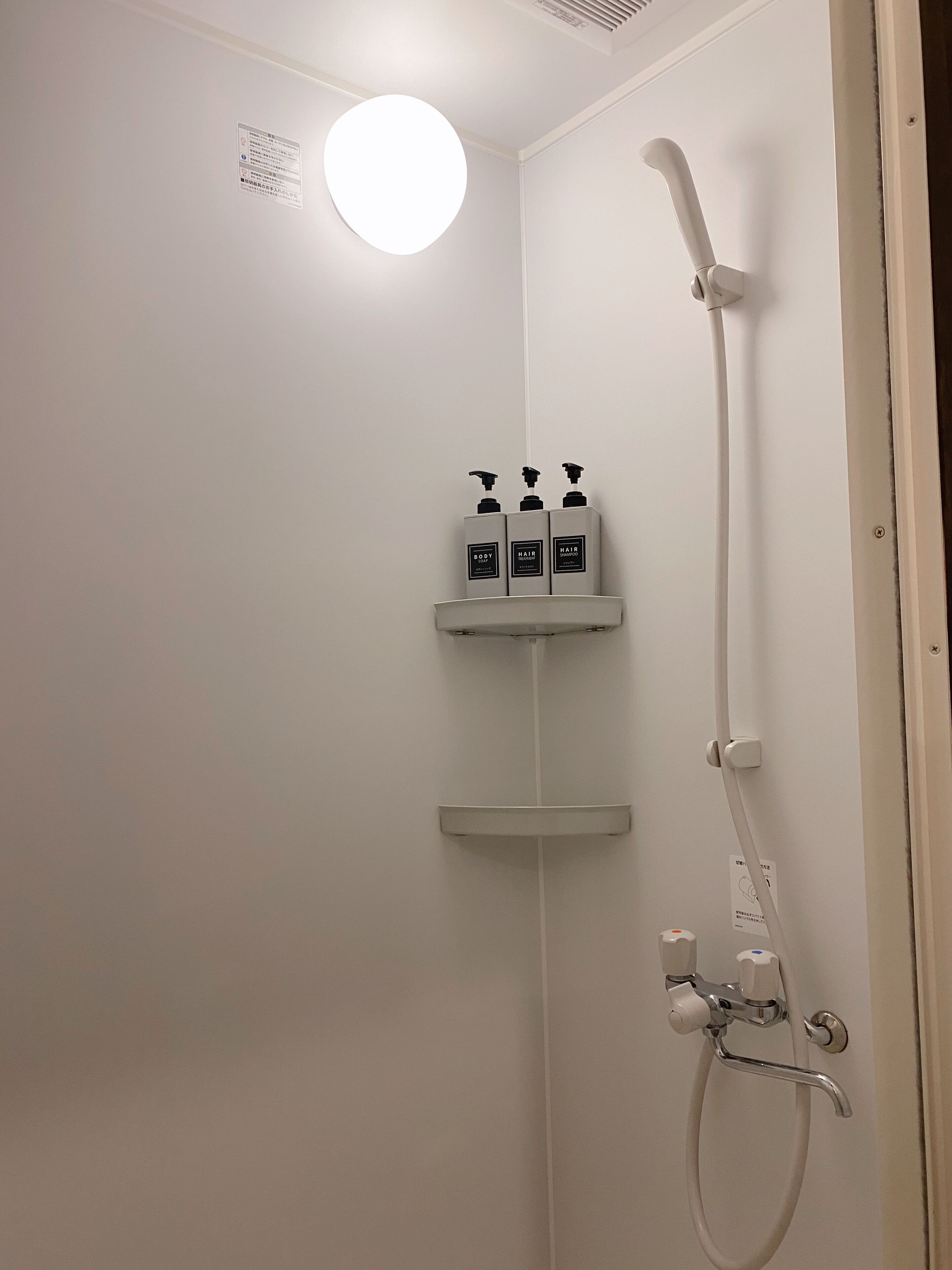 A shower with a handheld showerhead, a wall-mounted faucet, and a shelf with three bottles of shampoo and conditioner.