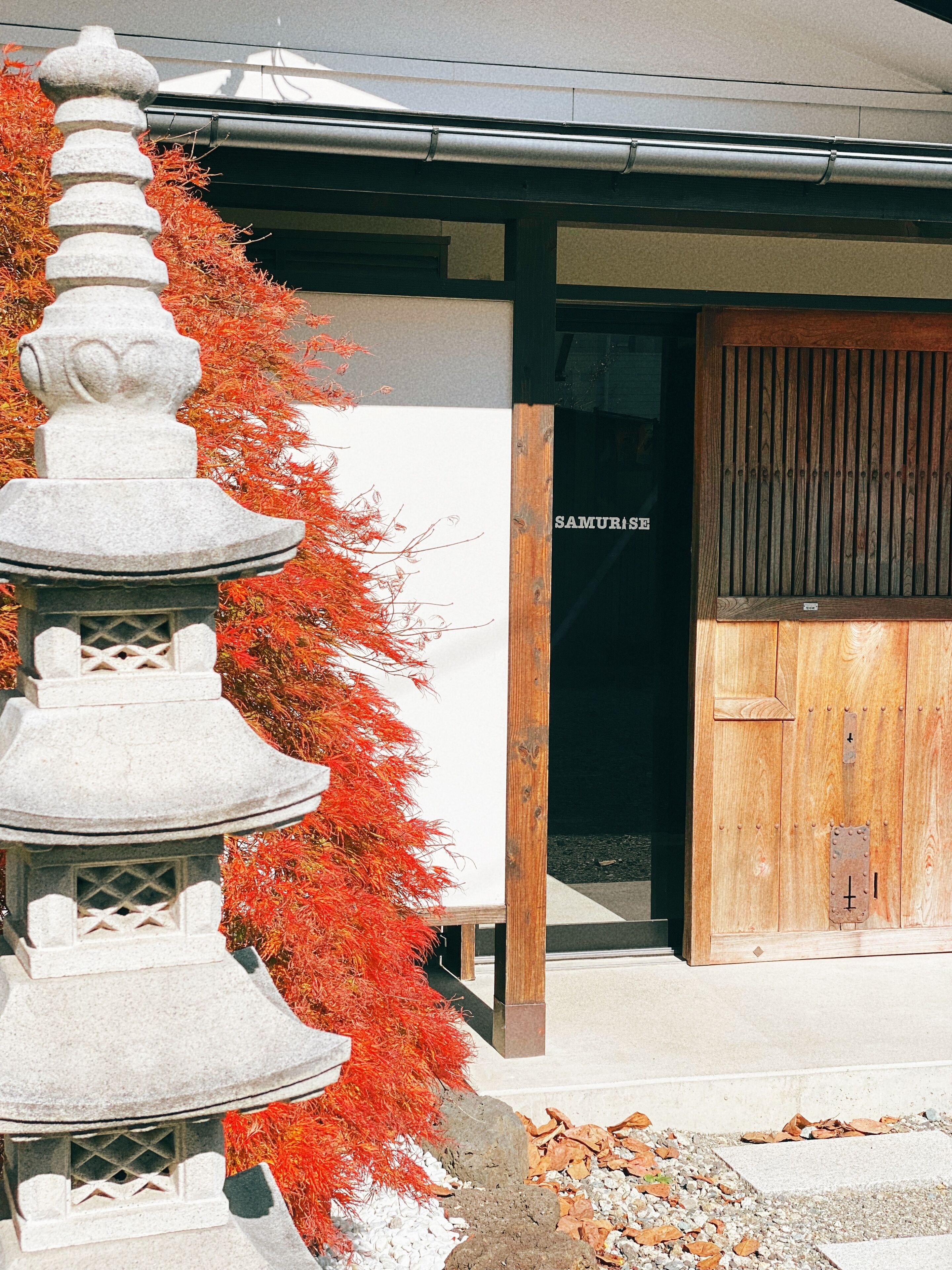 Un farolillo de piedra japonés tradicional, un edificio de madera con un letrero que dice "SAMURISE" y una puerta de madera.