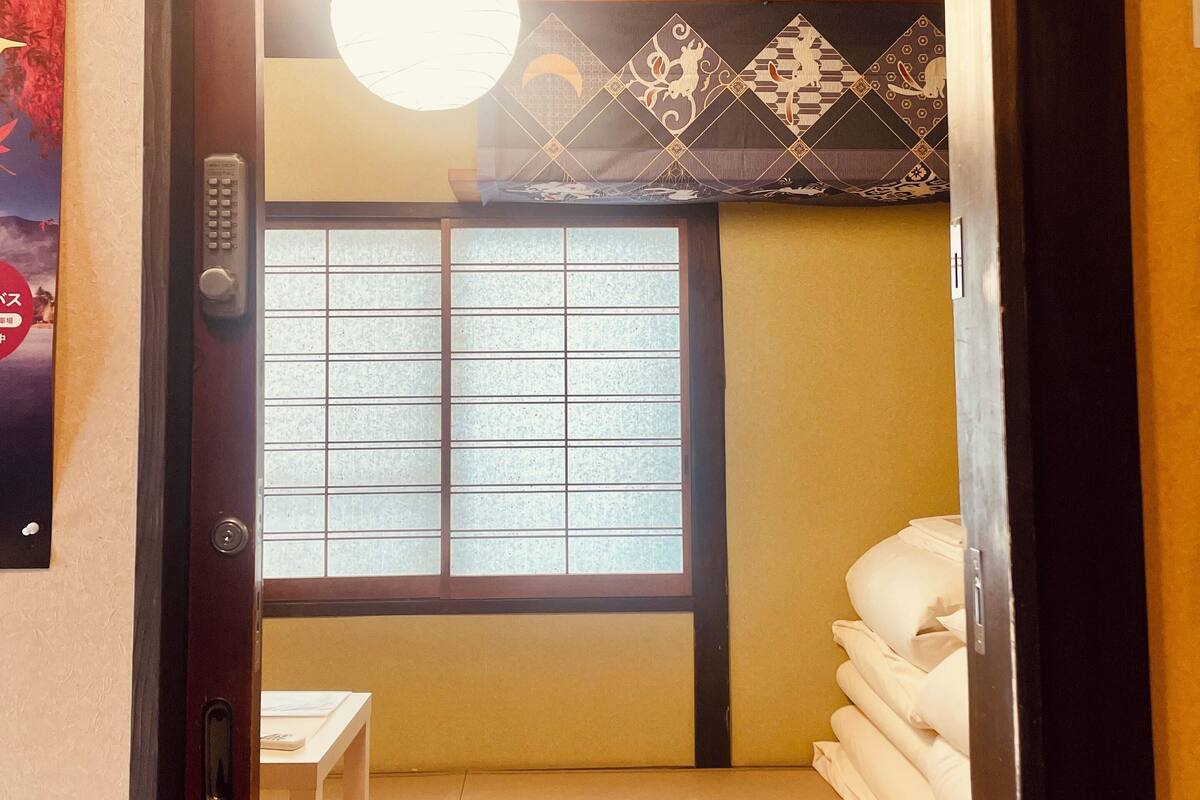 Ein traditioneller japanischer Raum mit Tatami-Bodenbelag, einem Futonbett, einem kleinen Tisch und einer hängenden Leuchte.