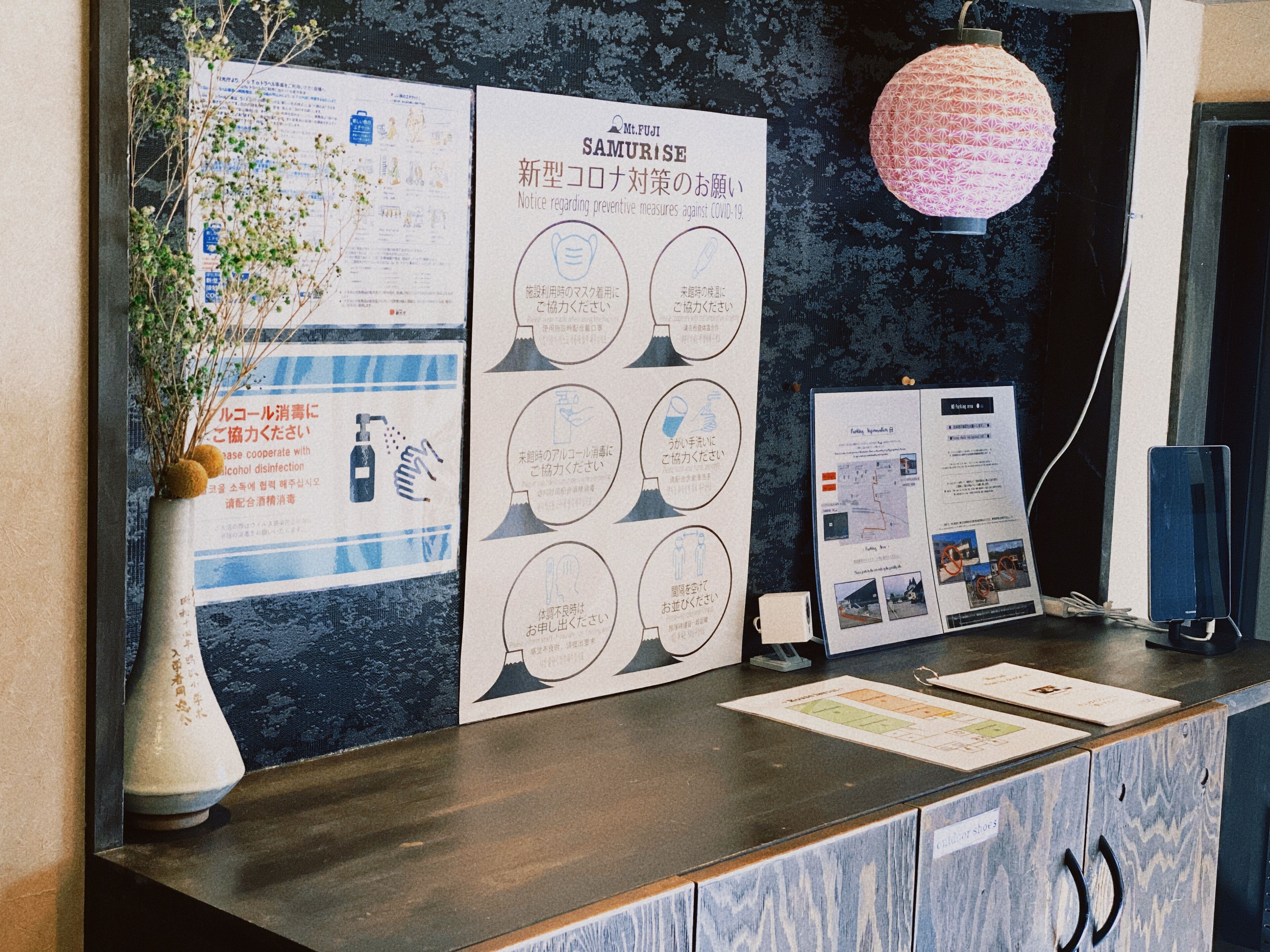 A reception desk with informational posters, a vase with dried flowers, and a hanging decorative light.