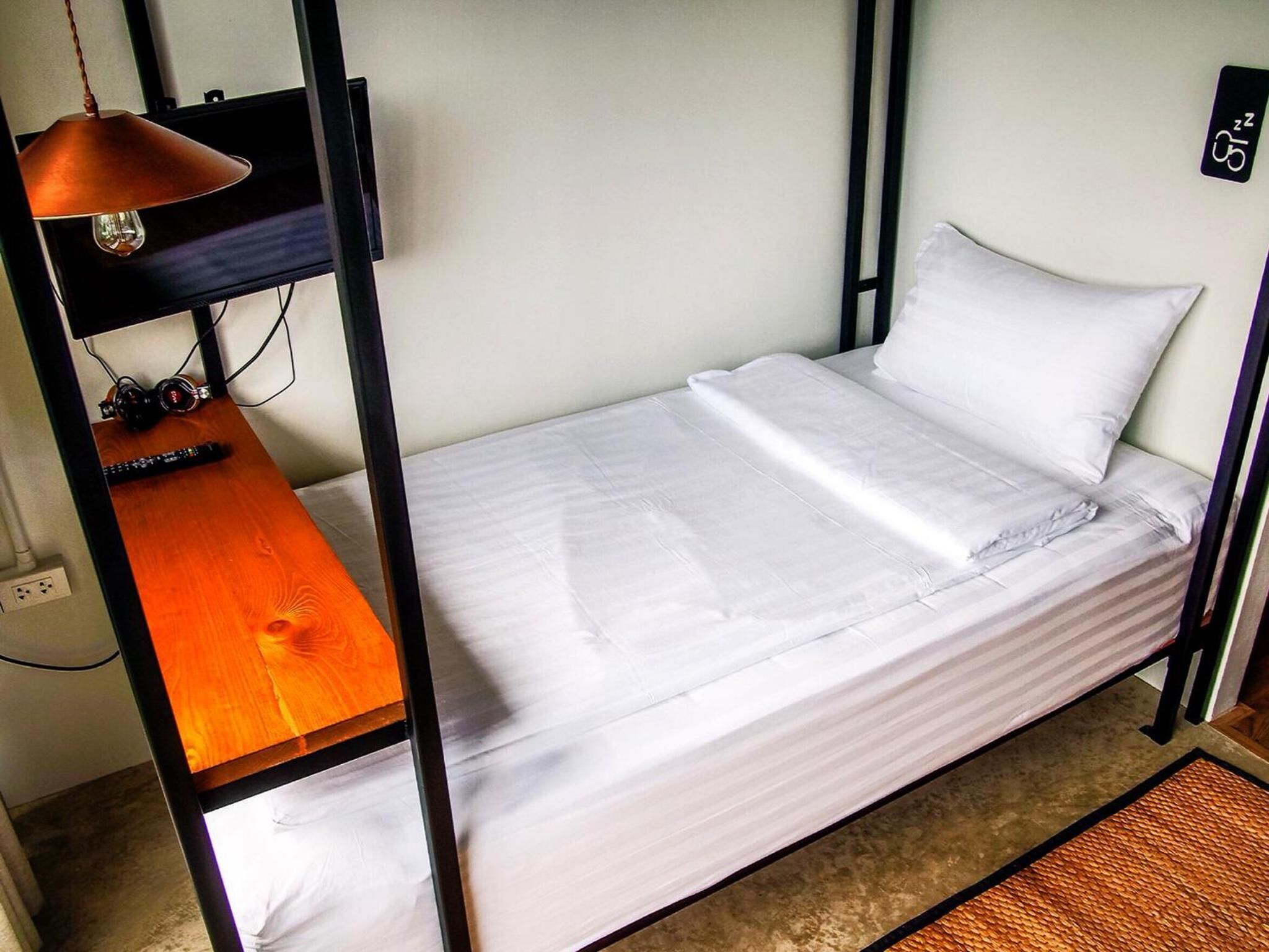A compact bed with a wooden side table and a hanging lamp in a small room.