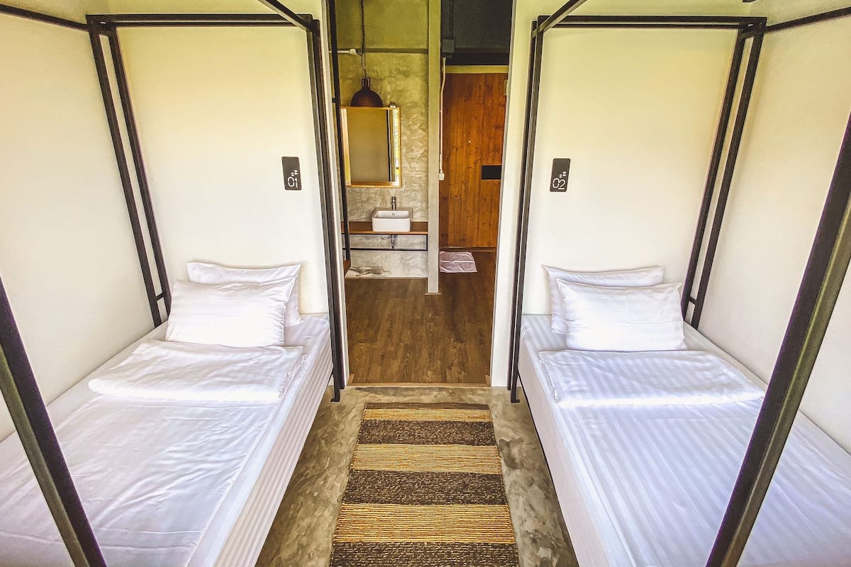 A corridor leading to two single beds with a bathroom and a mirror in the background.