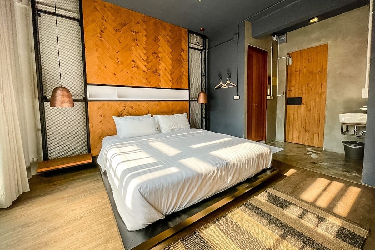 A modern bedroom with a large bed, a wooden accent wall, and a view of the bathroom.