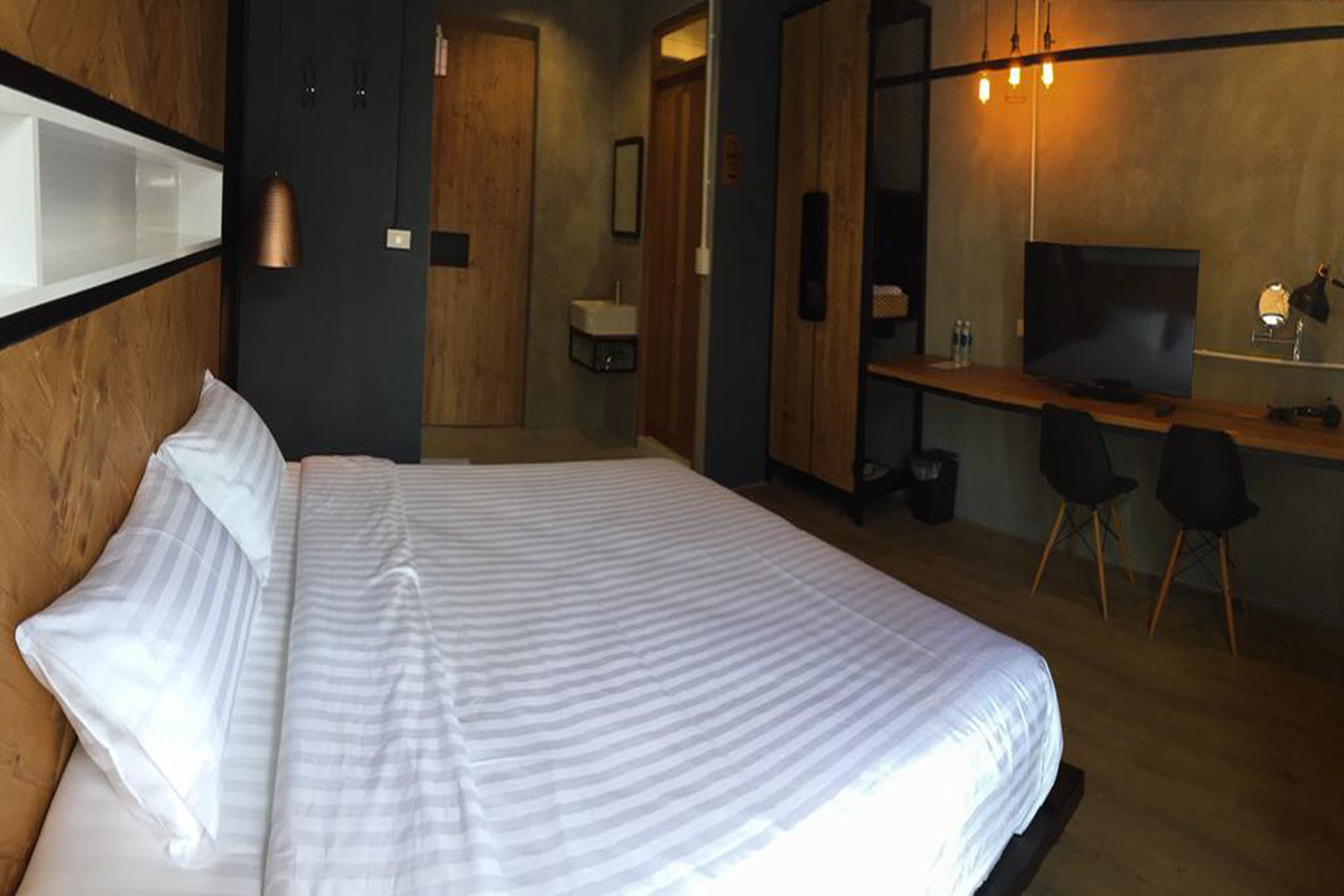 A modern hotel room with a large bed, a desk, a television, and a small bathroom.