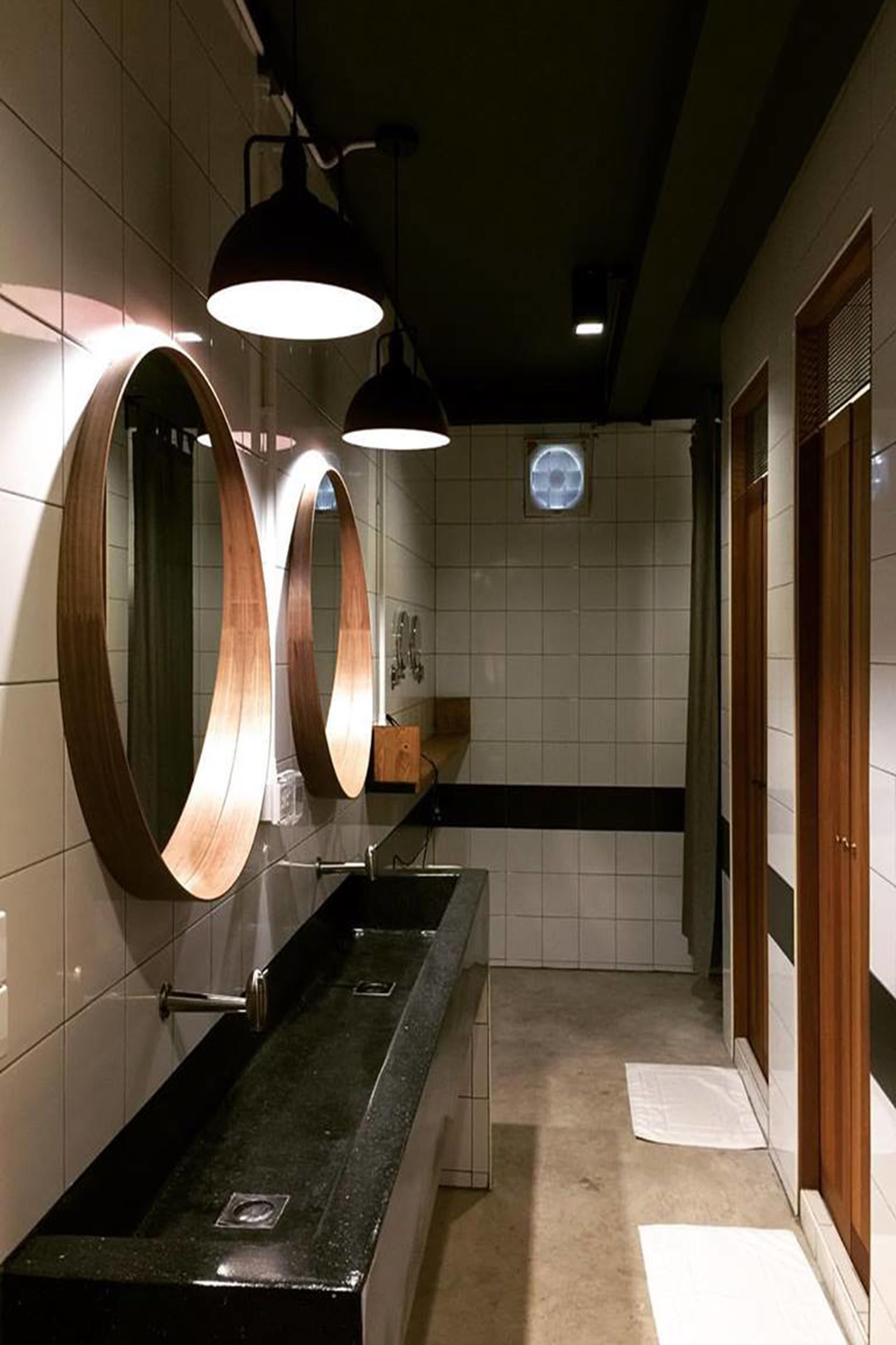 Un baño moderno con encimera negra, tres espejos grandes y dos lámparas colgantes.