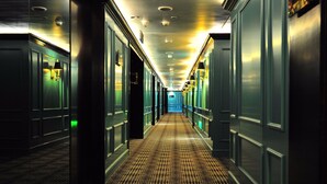 Un corridoio d'albergo con pavimento decorato, illuminazione a incasso e porte su entrambi i lati.