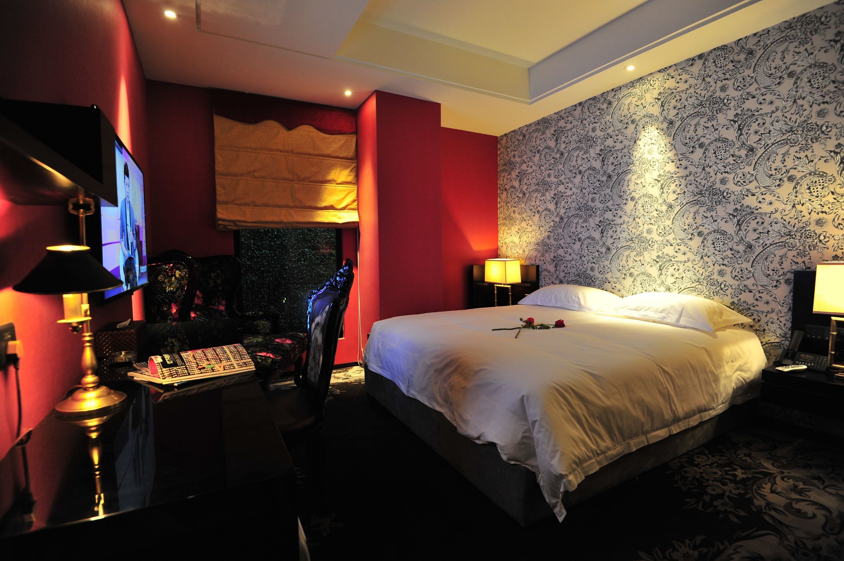 A hotel room with a large bed, a desk with a computer, a TV, and a lamp.