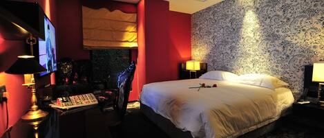 A hotel room with a large bed, a desk with a computer, a TV, and a lamp.