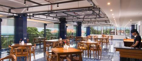 A spacious restaurant with high ceilings, wooden tables and chairs, and large windows offering views of the outdoors.