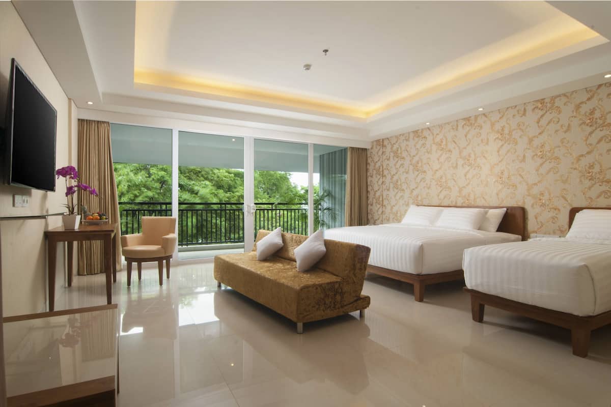 A hotel room with a large bed, a sofa, a TV, and a balcony with a view of greenery.