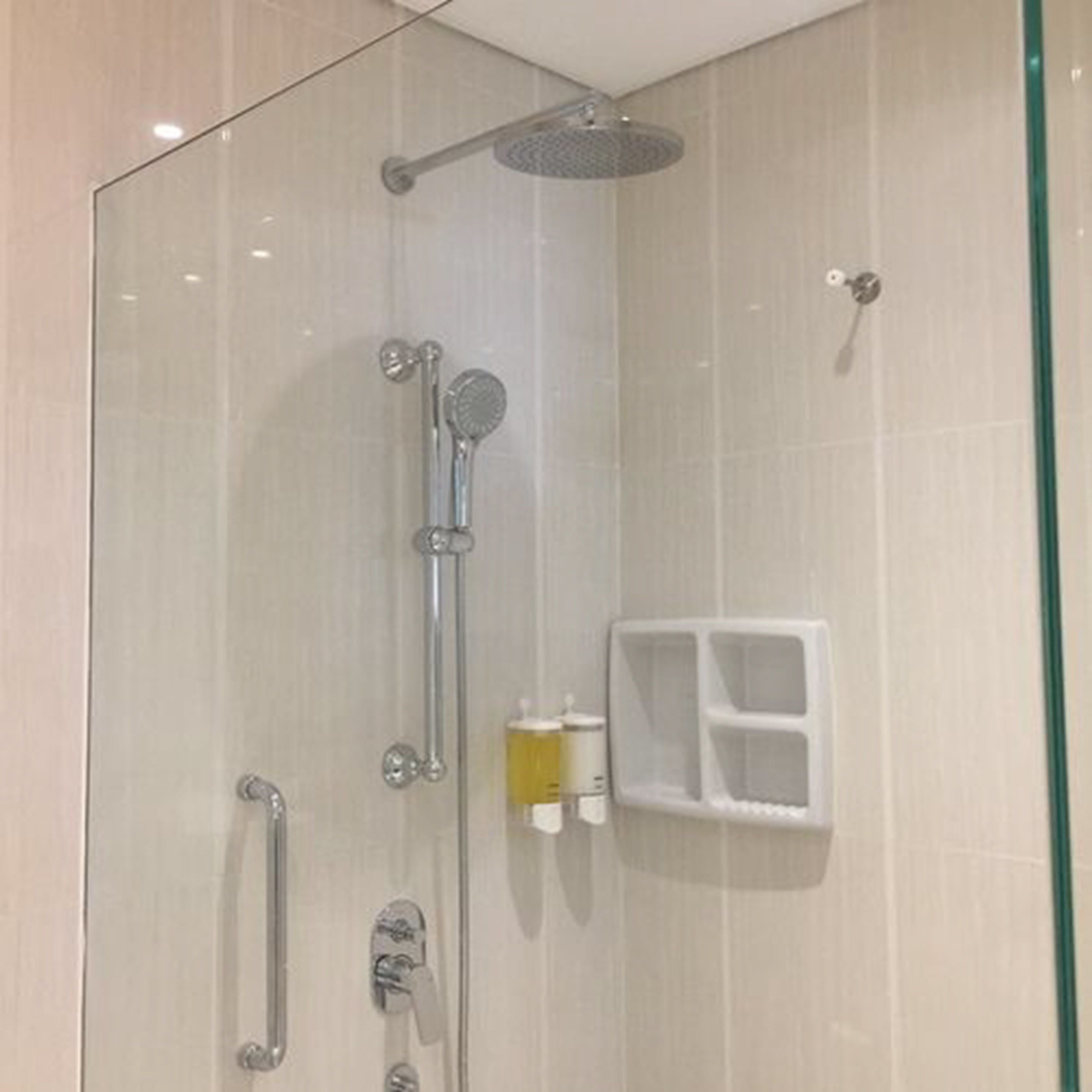 A glass-enclosed shower with a handheld showerhead, a handheld showerhead, and a wall-mounted showerhead.