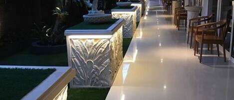 Un couloir doté d’un sol réfléchissant, une rangée de chaises et un mur décoratif orné d’une plante.