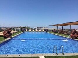 A swimming pool with two bronze animal statues on either side, surrounded by lounge chairs and a clear view of buildings in the background.