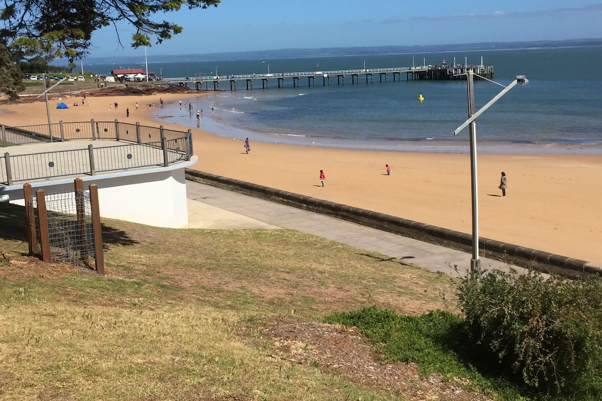 A beach with a wooden walkway, a pier, and a clear view of the ocean.