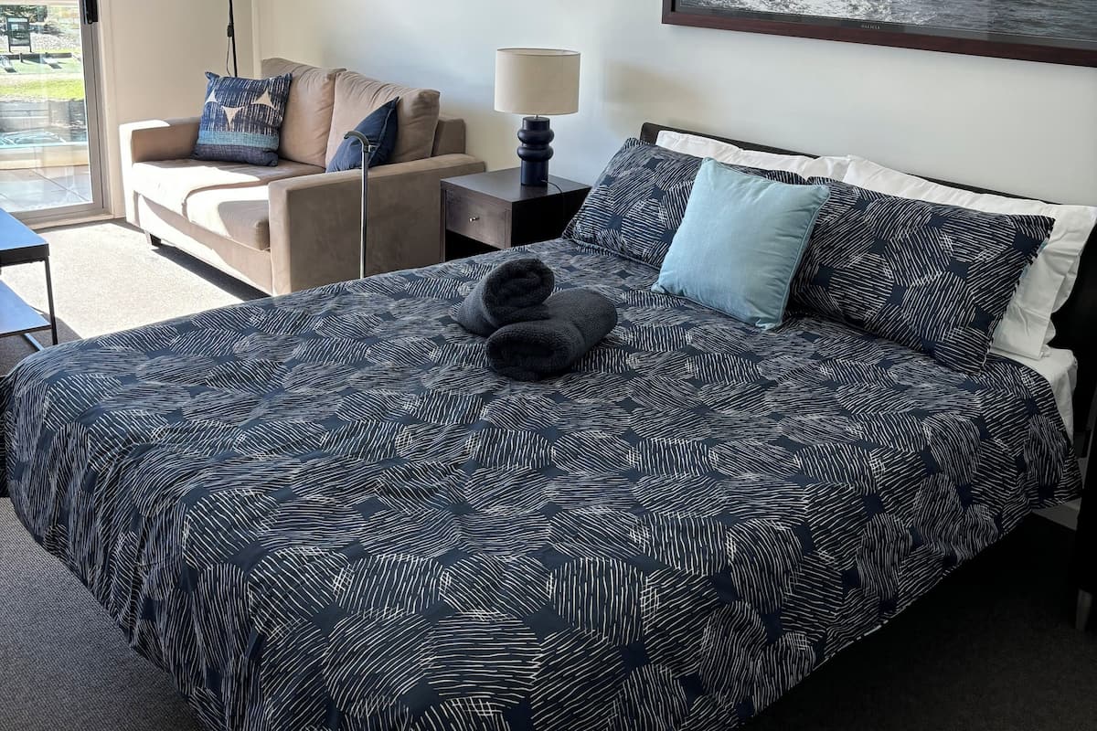 A hotel room with a large bed, a sofa, a desk, and a view of the sea.