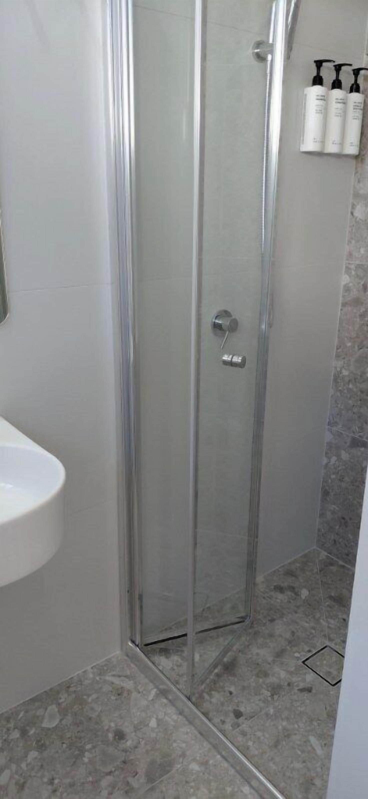Un baño con cabina de ducha de vidrio, lavabo blanco y artículos de aseo en la pared.