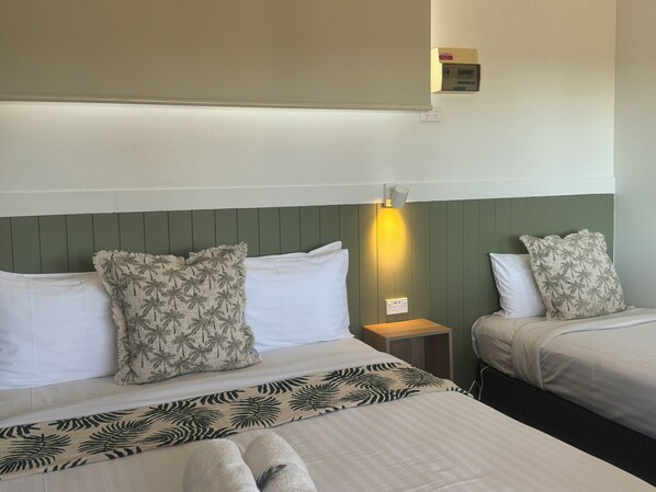 Habitación de hotel con dos camas, una mesita de noche, una lámpara fijada a la pared y un termostato.