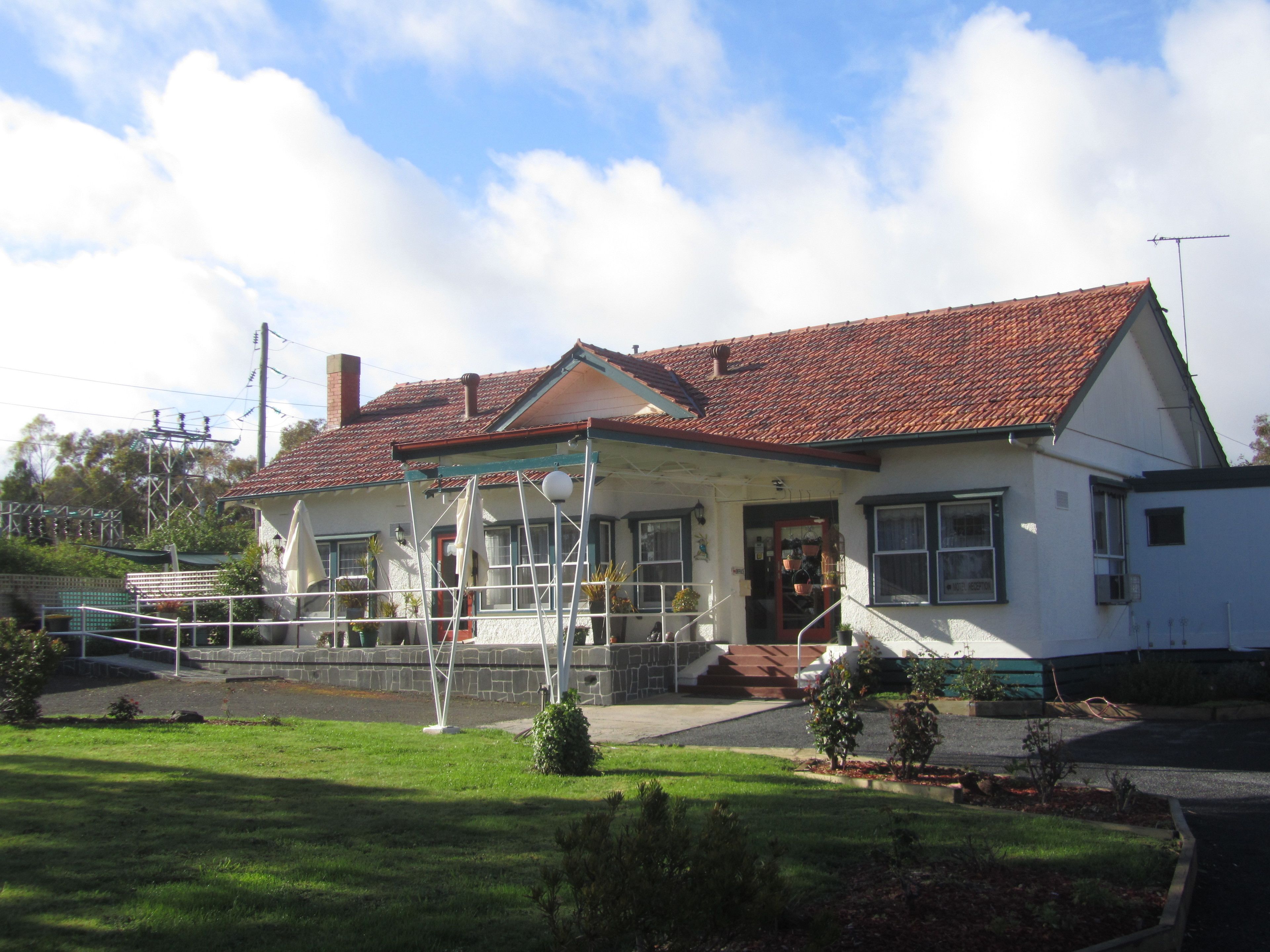 A two-story house with a red-tiled roof, a covered porch, and a small front yard with a lawn and a few potted plants.